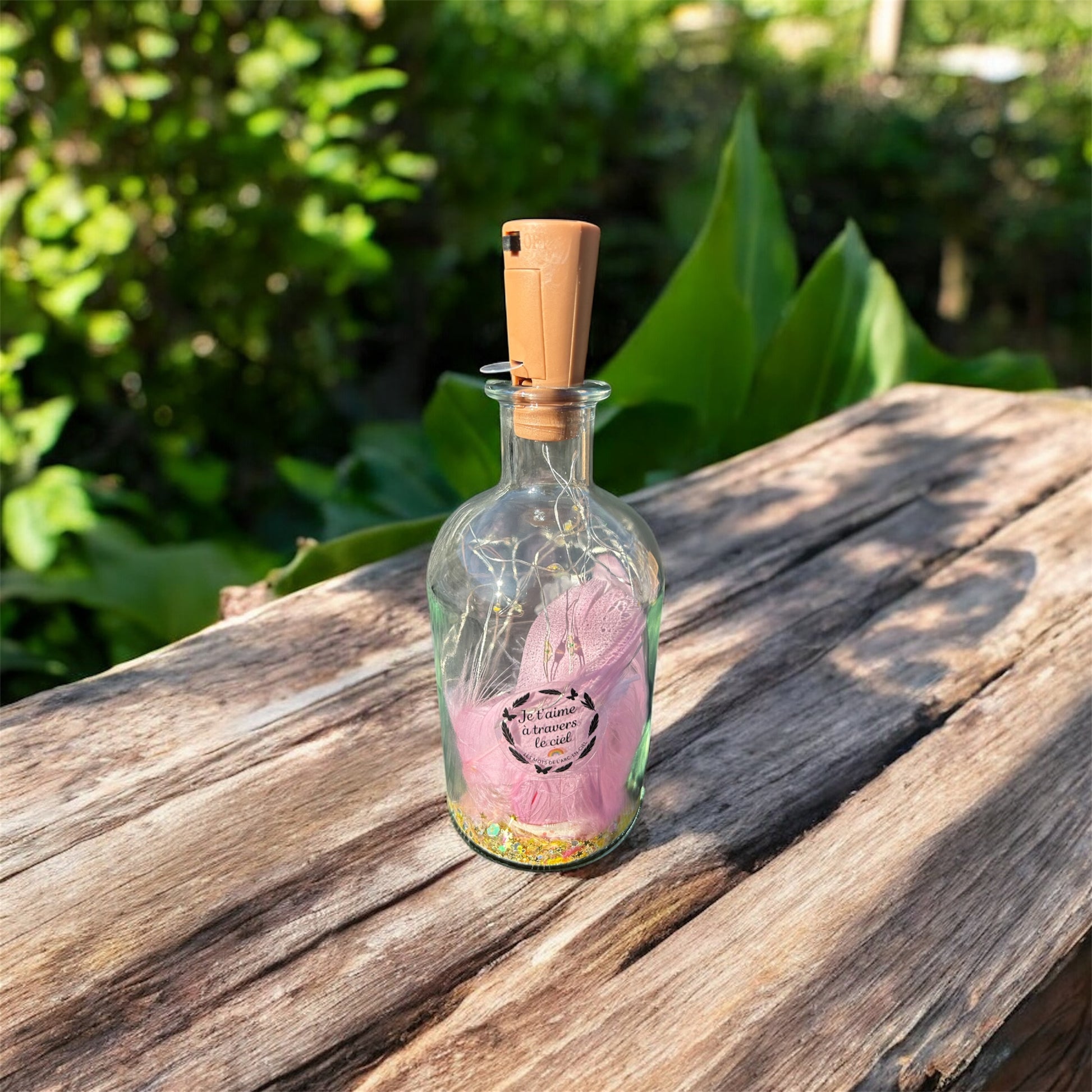 Bouteille lumineuse souvenir posée sur une table en bois au soleil, remplie de petites lumières et décorée d’un message symbolique — création destinée à honorer la mémoire d’un animal.