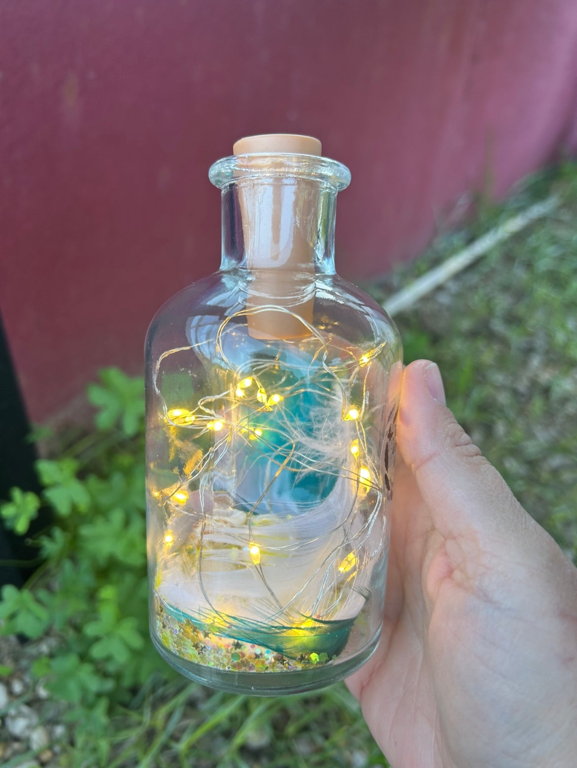 Bouteille lumineuse souvenir posée sur une table en bois au soleil, remplie de petites lumières et décorée d’un message symbolique — création destinée à honorer la mémoire d’un animal.
